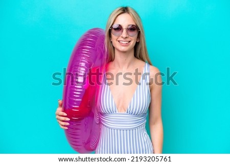 Blonde woman in swimsuit holding an air mattress donut isolated on blue background smiling a lot