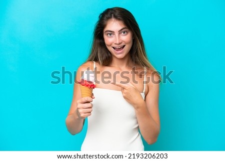 Young woman in swimsuit holding an ice cream isolated on blue background and pointing it