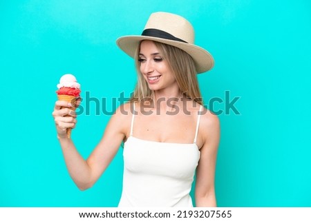 Blonde woman in swimsuit holding an ice cream isolated on blue background with happy expression