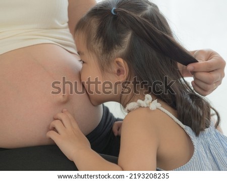 Close up little girl kissing on pregnant mother's tummy. Sister's love and bonding.