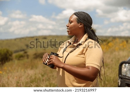 Side view of emale tour guide using binoculars and searching the landscape for wildlife in Africa Royalty-Free Stock Photo #2193216997