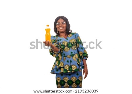 beautiful african woman in traditional dress standing over white background showing bottle of fruit juice smiling. Royalty-Free Stock Photo #2193236039