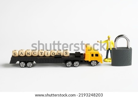 Toy truck with a trailer and word sanction stopped next to a man with a ban and a padlock. White background. Concept of trade sanctions and customs blocking the delivery of goods. Close-up
