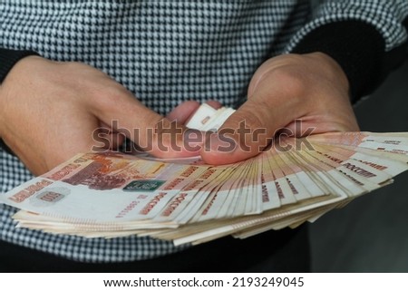 Close-up of men's hands holding a fan of Russian money in five-thousand-dollar bills.