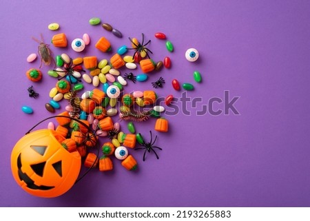 Halloween concept. Top view photo of pumpkin basket with candies eyeballs insects cockroach centipedes and spiders on isolated violet background