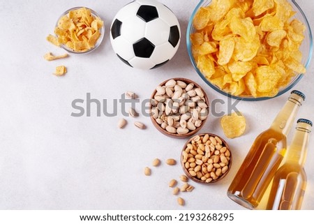 Beer and snack on gray table top with football ball, football game night food, copy space. Snack and drink for watching football games and championships
