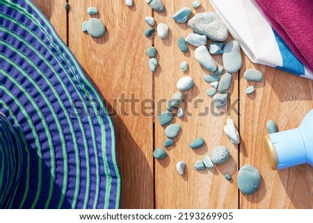 Big blue hat, marine bag, cream and blue pebbles on the wooden table. Summer relaxation backgrounds and flat lay