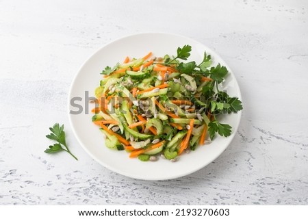 A plate with a salad of cucumbers, carrots, celery, seeds and parsley on a light blue background. Delicious healthy homemade food