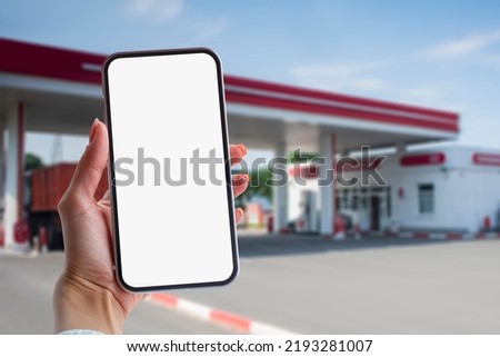 Woman holds a close-up of a smartphone with a white screen in his hands against the backdrop on a gas station. Technology mockup for apps and websites