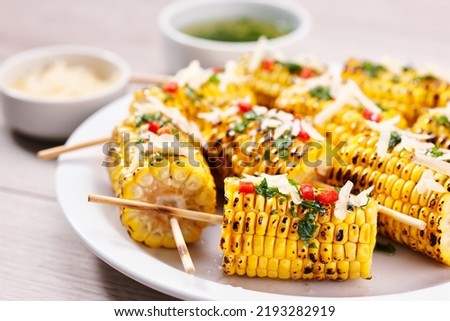 Grilled corn on cob sprinkled with cilantro and grated parmesan in a white dish on a table, close up. Royalty-Free Stock Photo #2193282919