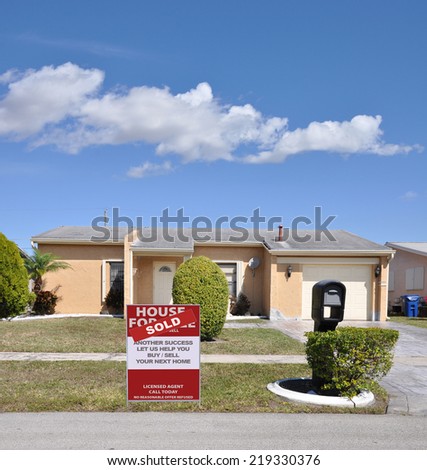 Sold (another success let us help you buy sell your next home) real estate sign curb of ranch style suburban home in residential neighborhood blue sky clouds