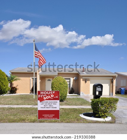 American Betsy Ross Flag Pole and Sold (another success let us help you buy sell your next home) real estate sign curb of ranch style suburban home in residential neighborhood blue sky clouds