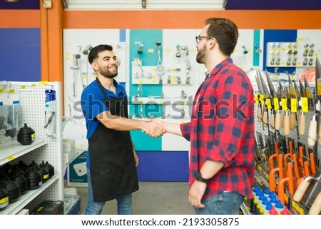 Cheerful male employee smiling shaking hands with a young man and greeting him to the hardware store during his shopping Royalty-Free Stock Photo #2193305875