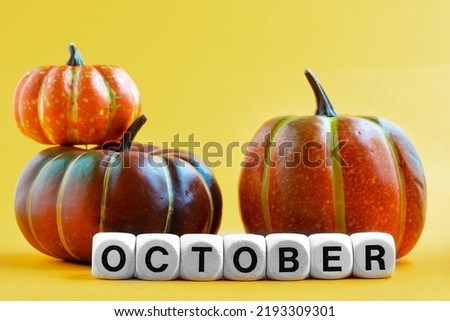 Miniature pumpkins and the word October assembled from wooden blocks Yellow background