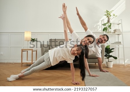Asian Thai parents and daughter fitness training exercise and practice yoga on living room floor, lovely rowing together for health and wellness, and happy domestic home lifestyle on family weekend.