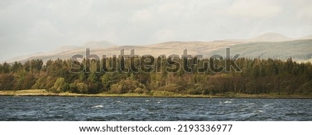 Panoramic view of the rocky river shores from the water. Trees, hills and mountains in the background. Cloudy blue sky. Gare Loch, Firth of Clyde, Scotland, UK Royalty-Free Stock Photo #2193336977
