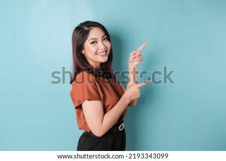 A portrait of a happy Asian woman is smiling and pointing copy space beside her, isolated blue background  Royalty-Free Stock Photo #2193343099