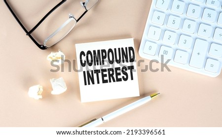 COMPOUND INTEREST text on a sticky with pen ,calculator and glasses on beige background