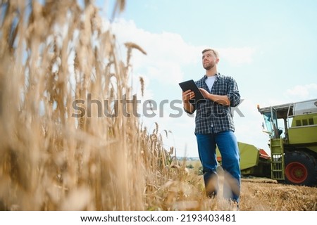 Handsome farmer with tablet standing in front of combine harvester during harvest in field Royalty-Free Stock Photo #2193403481