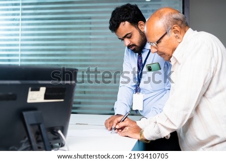 Focus on banker, Employee helping or guiding old man to fill receipt or to fill banking documents at desk - concept of client agreement, elderly support and banking customer service.