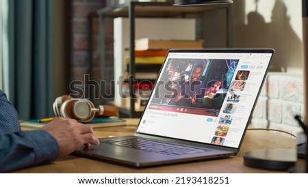 Close Up on Male Hands Using Laptop to Watch Video Sharing Service Mock-up Where African American Influencer Talks About Lifestyle. Interface with Related Streams, Likes, Comments. Royalty-Free Stock Photo #2193418251