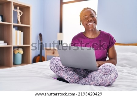 African american woman using laptop sitting on bed at bedroom