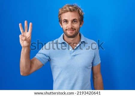 Caucasian man standing over blue background showing and pointing up with fingers number three while smiling confident and happy. 