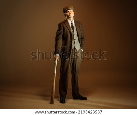 Peaky blinders style. Young man in image of english gangster, businessman wearing suit and cap standing isolated over dark vintage background. Concept of business, personality, emotions, fashion Royalty-Free Stock Photo #2193423537