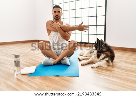 Young hispanic man stretching with dog at sport center