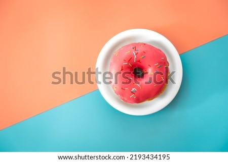 Donut in pink icing on a colored background, flat lay.