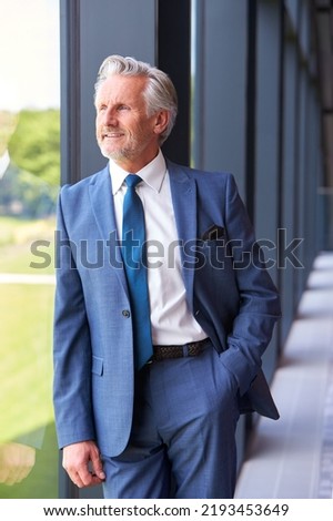Portrait Of Smiling Senior Businessman CEO Chairman Standing By Window Inside Modern Office Building Royalty-Free Stock Photo #2193453649