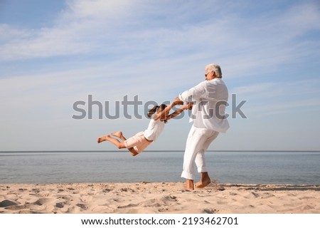 Cute little girl with grandfather spending time together on sea beach Royalty-Free Stock Photo #2193462701