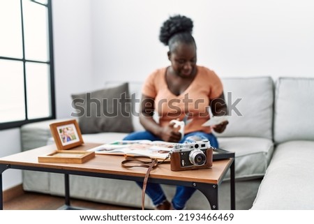 Young african american woman looking photobook sitting on sofa at home