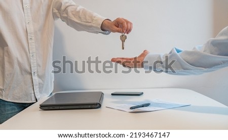 Detail of the hands of the agent giving the keys to the buyer, in the real estate agency. Horizontal photography with copy space.