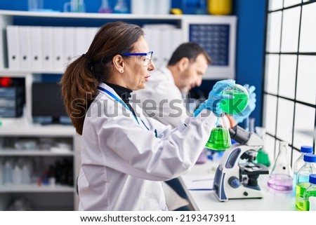 Middle age man and woman scientists measuring liquid at laboratory