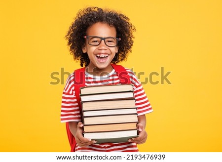 Funny african american boy in glasses hugging books and laughing at camera while studying at school against yellow background