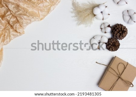 Brown gift box with cotton flowers, pine cones over the white wooden table. 