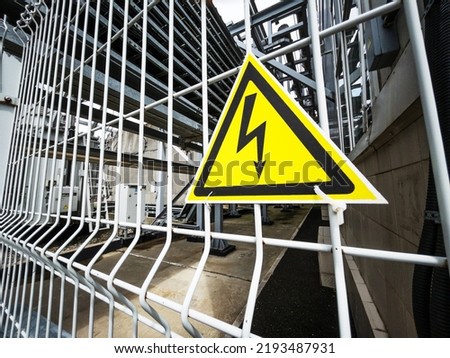 Danger Sign High voltage in the yellow triangle on the metal fence of the grid
