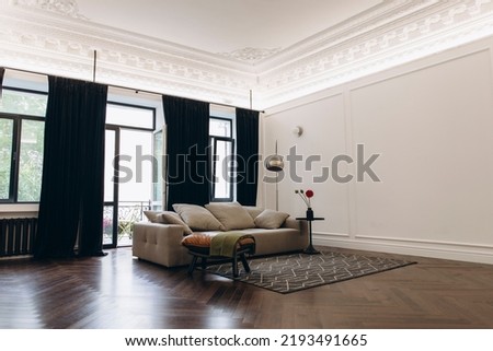 an example of a living room interior in a neo-classical style with modern elements. a sofa in the middle of a room with high ceilings and moldings. Royalty-Free Stock Photo #2193491665