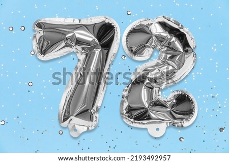 Silver foil balloon number, digit seventy two on a blue background with sequins. Birthday greeting card with inscription 72. Top view. Numerical digit. Celebration event, template. Royalty-Free Stock Photo #2193492957