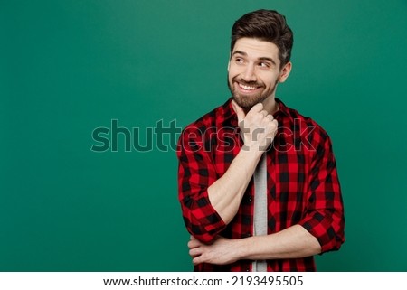 Young happy smiling fun cool man he 20s wear red shirt grey t-shirt look aside on workspace area mock up prop up chin isolated on plain dark green background studio portrait People lifestyle concept