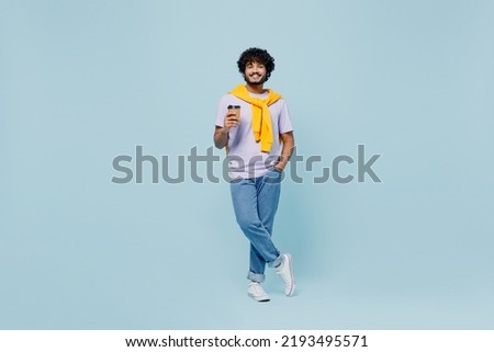 Full size cheerful young bearded Indian man 20s years old wears white t-shirt hold takeaway delivery craft paper brown cup coffee to go isolated on plain pastel light blue background studio portrait Royalty-Free Stock Photo #2193495571