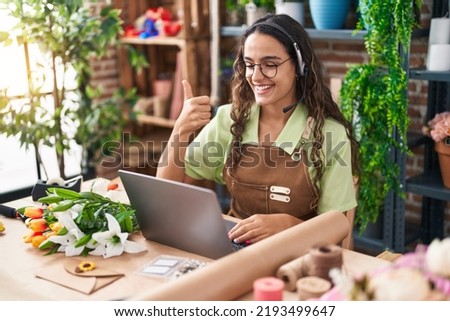 Young hispanic woman working at florist shop doing video call smiling happy and positive, thumb up doing excellent and approval sign 