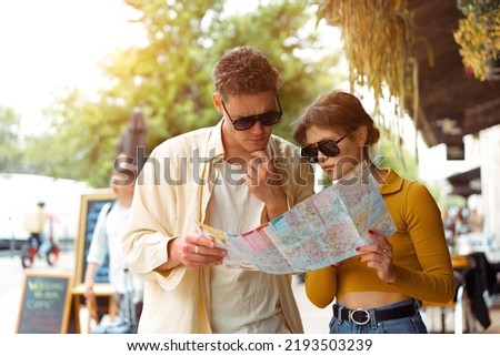 Tourist Couple With Map In Capital City Europe. Happy Young People Using Map, Traveling On Summer Vacations. Handsome Man And Beautiful Woman Having Trip Outdoors. High Quality Image.
