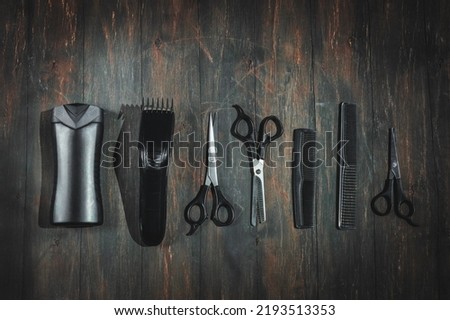 Scissors, combs, shampoo and a men's hair clipper lie in a row on a black wooden background, flat lay close-up. The concept of a male barbershop. Royalty-Free Stock Photo #2193513353
