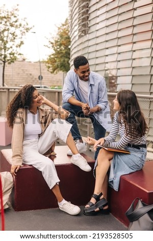 Group of different young students discuss something in campus park during day. Brunettes boy and girls wear casual clothes. Friends concept Royalty-Free Stock Photo #2193528505