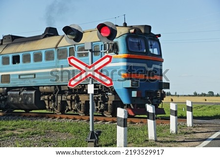 Forbidding red traffic light and roadsign on one way railway crossing on move old train locomotive background on countryside at summer day