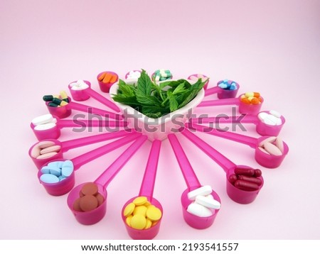                   pills, tablets, capsules in pink spoons and plant inside heart in center                                