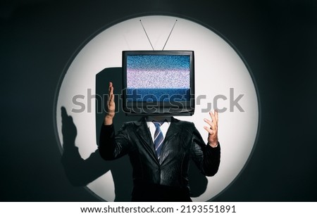 Man with TV instead of head. Media zombie concept with television addicted male in black coat with crossed arms posing on studio in the spotlight. Conceptual, contemporary art collage. Surrealism Royalty-Free Stock Photo #2193551891