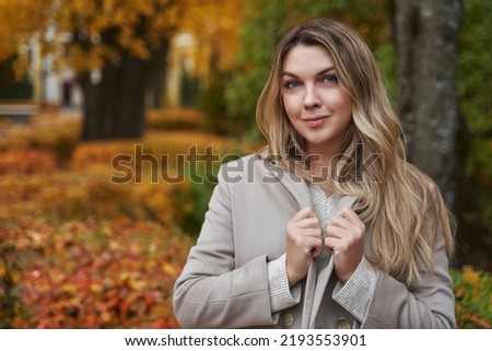 portrait of a beautiful woman in the autumn park raised the collar of her light coat. yellow trees and fallen leaves.